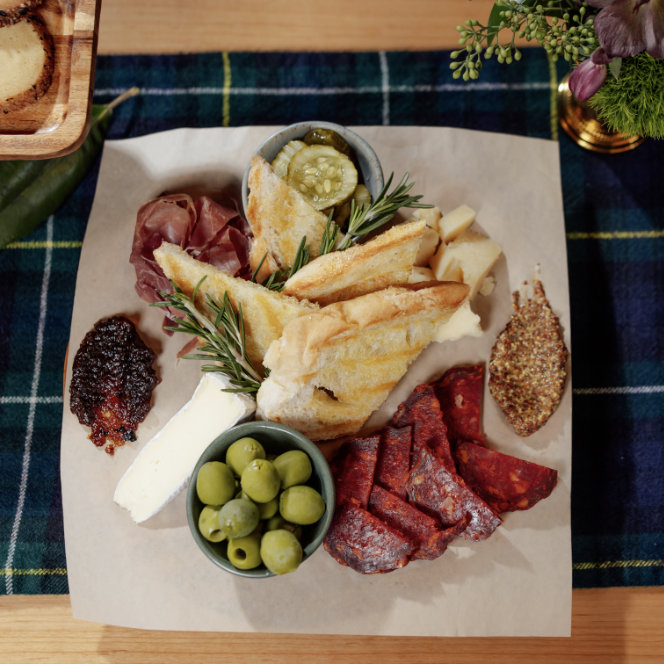 An assortment of gourmet foods, including slices of cured meats, two types of soft cheeses, and dollops of mustard and fig jam with toasted bread slices.