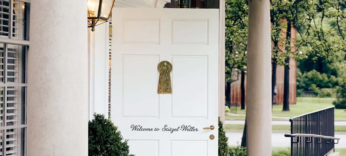 A white door at the entrance of the Stitzel-Weller Distillery, adorned with a large brass keyhole sculpture and hanging keys.