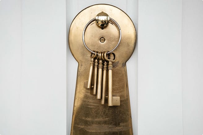 A large brass keyhole sculpture mounted on a wall, with a ring holding five ornate brass keys hanging from it.