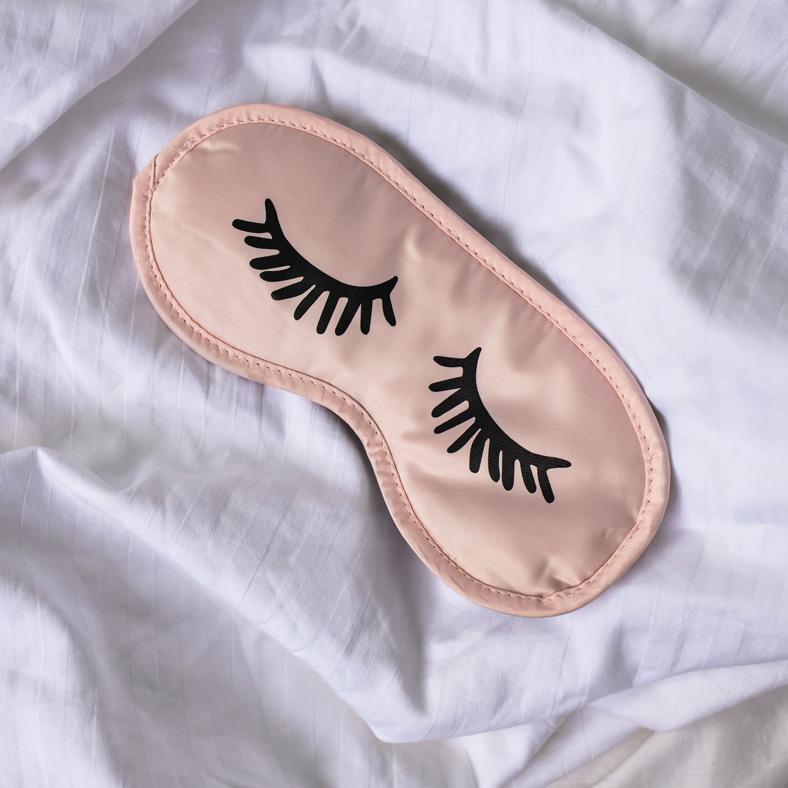 Pink sleep mask with embroidered eyes on a bed