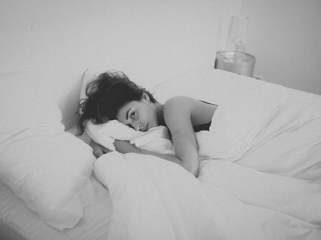 Woman in a bed with bare arm and messy hair trying to sleep.