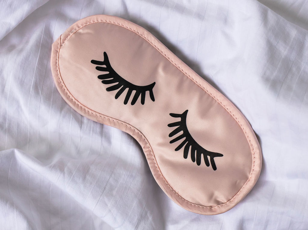 Pink sleep mask with embroidered eyes on a bed
