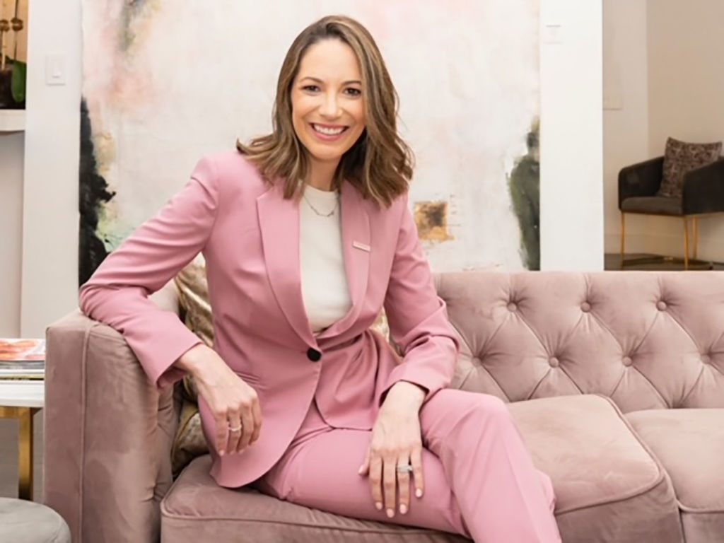 Stephanie Cartin seated on a velvet sofa in a pink suit. 