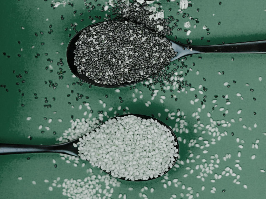 Sesame and Chia seeds in spoons and scattered on a green background.