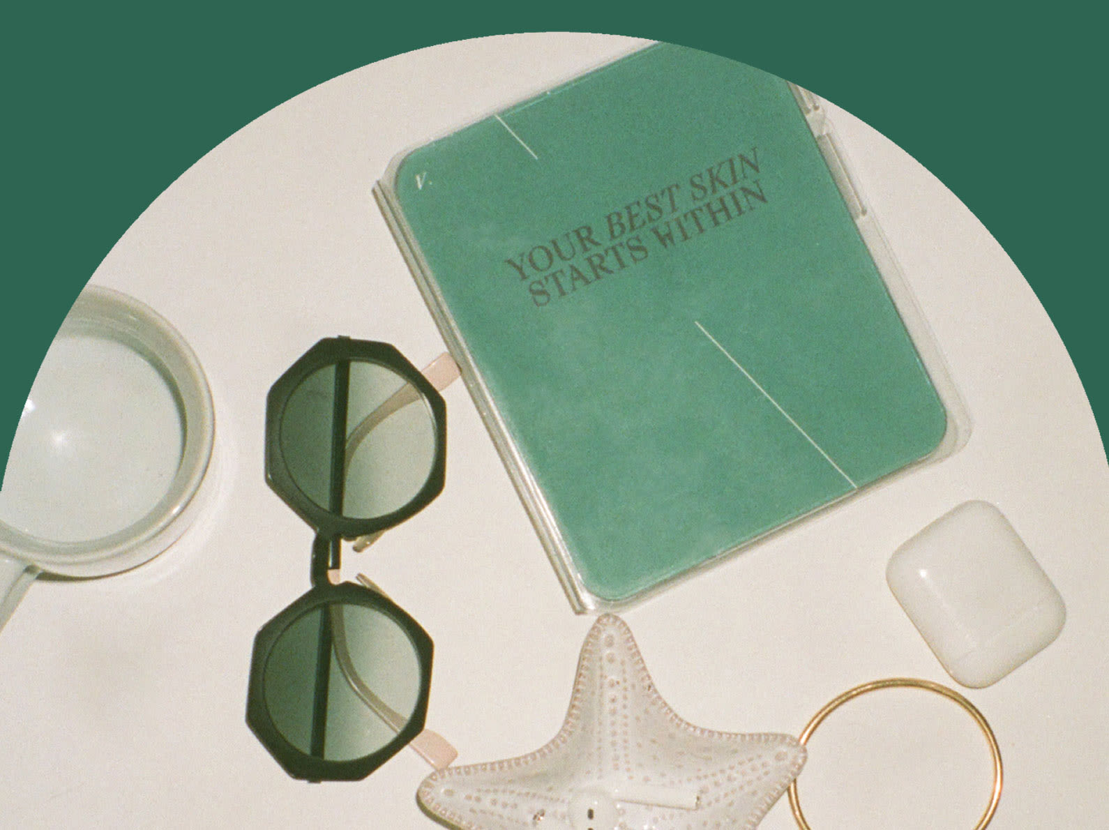 Veracity skin and health test kit with sunglasses, coffee mug, gold bangle, and airpods in a starfish dish.
