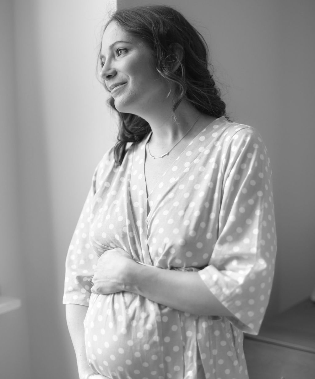 Stephanie Cartin holding her pregnant belly in a black and white photograph.