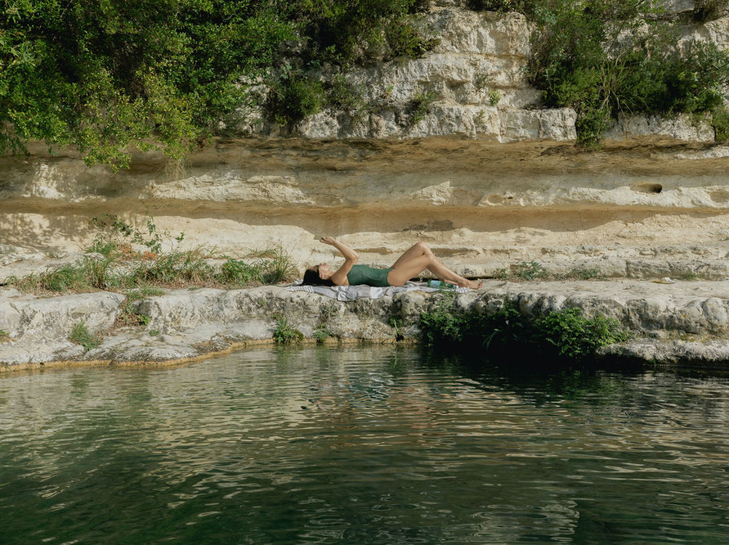 Woman lying in the sun my a lake in a green bathing suit.