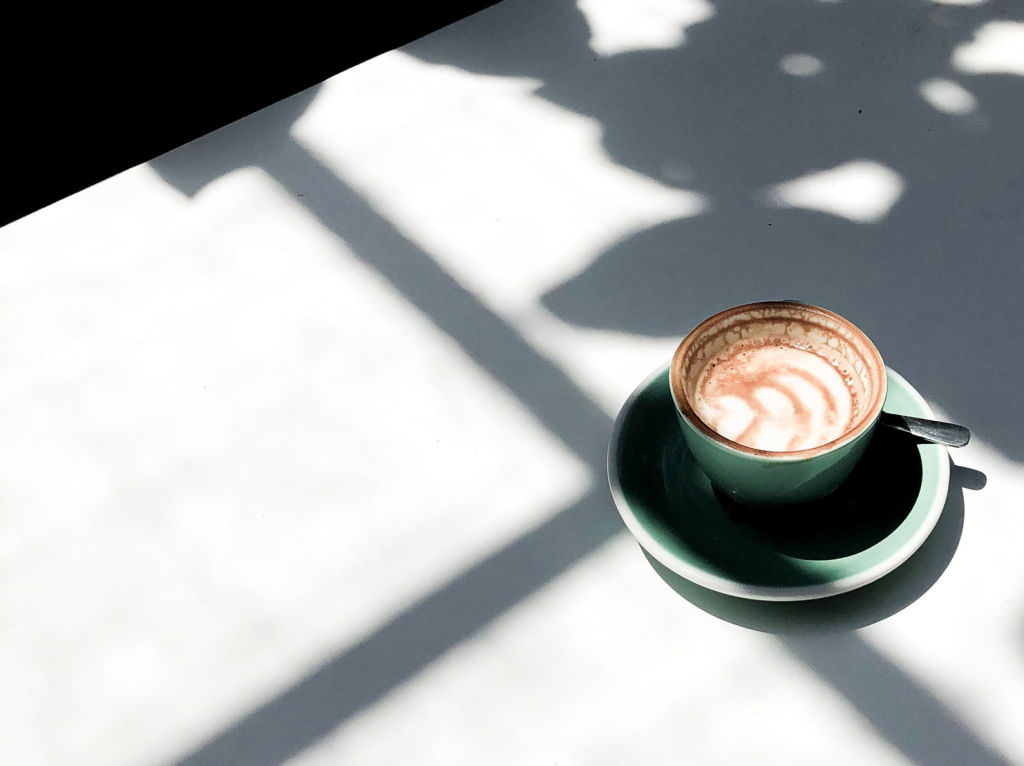 A cappuccino in a green cup with sunlight and shadows