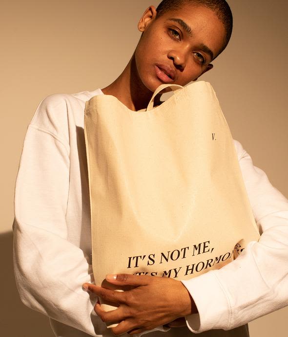 Woman carrying white It's Not Me It's My Hormones tote with black lettering