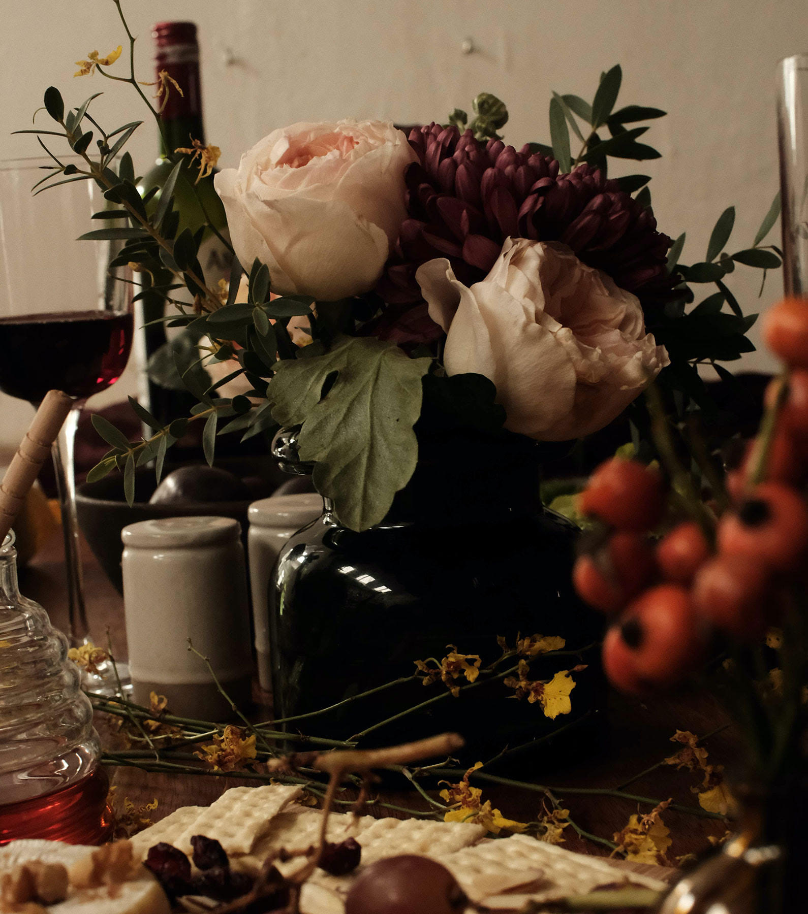 Table setting with light pink roses, berries, and greenery, crackers, and red wine. 