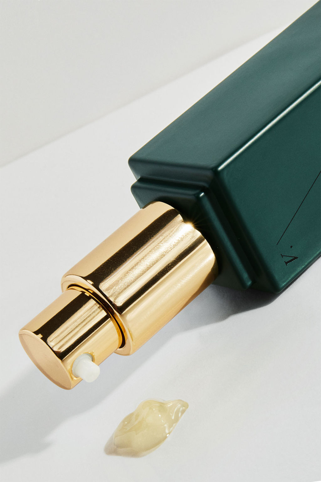 Green serum bottle with gold pump uncapped with droplet of product