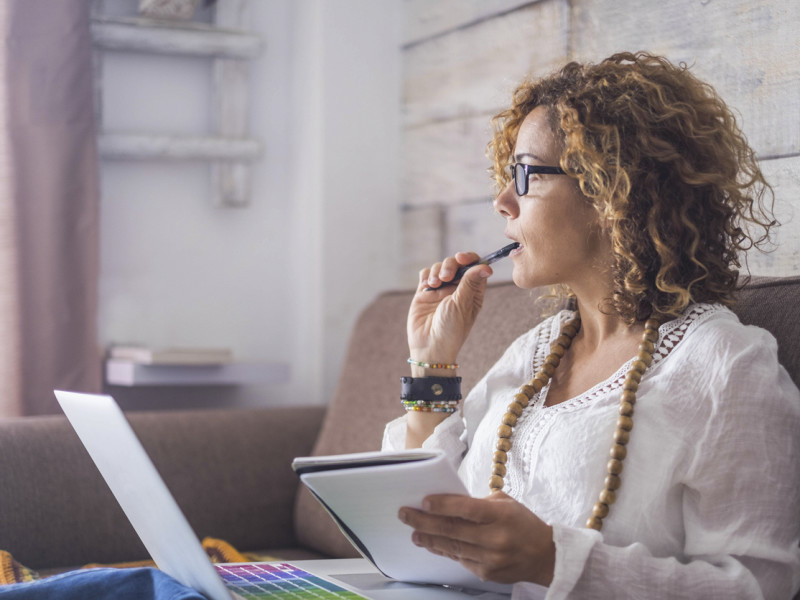 Woman with pen in her mouth ponders over a notebook