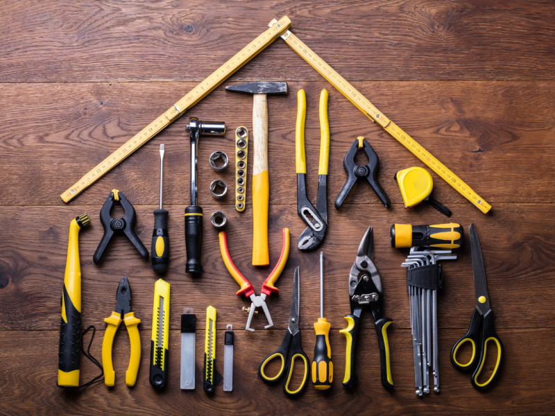 Yellow and black tools arranged in the shape of a house on a dark wood table.