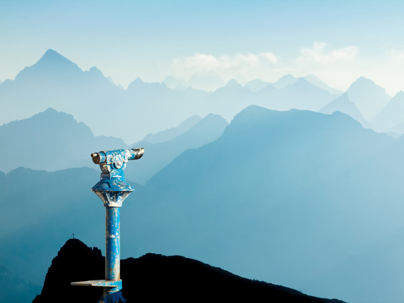 Beat-up blue standing monocular overlooking a blue mountain range.