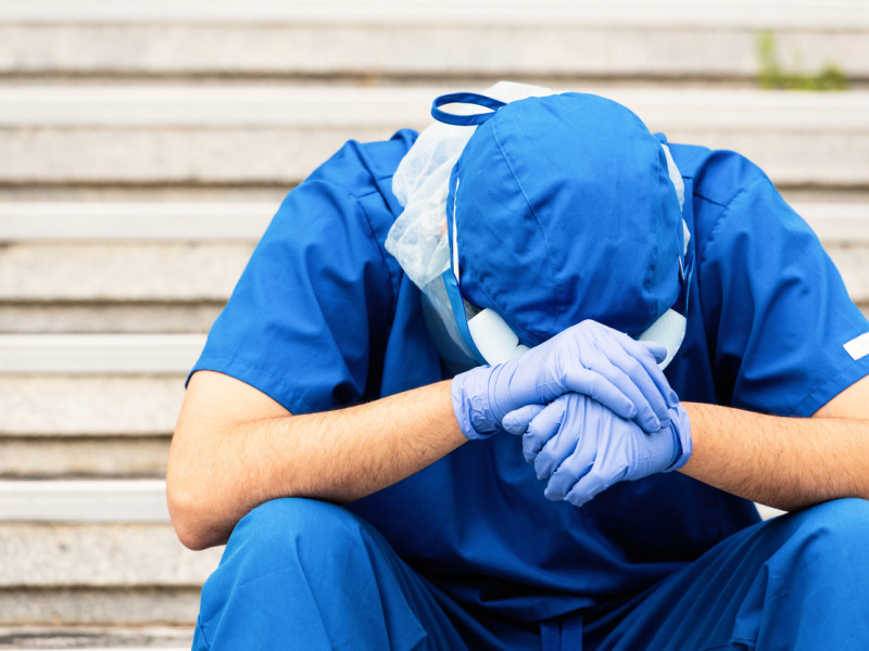 压力很大的男性医护人员，穿着蓝色工作服，戴着帽子，头戴在手上