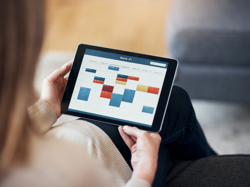 Blonde woman with long hair checking her weekly work schedule with colorful meeting blocks on her tablet.