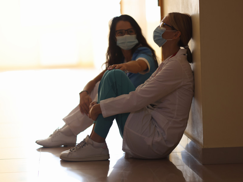 Tired women doctors are sitting in masks in corridor. Burnout of healthcare workers concept