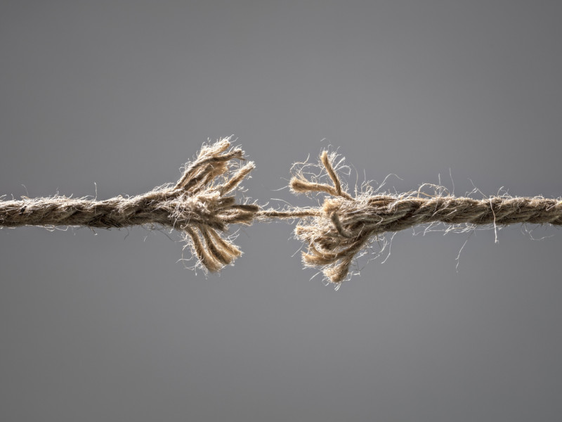 Two pieces of frayed rope connected by a single thread 
