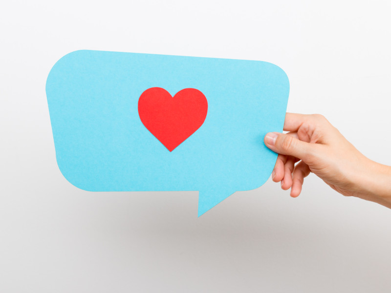 Hand holding a blue speech bubble with a red heart inside