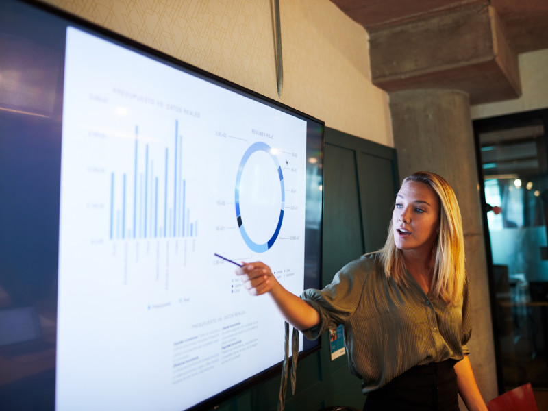 Young blonde businesswoman presenting financial results via a TV screen during a meeting.