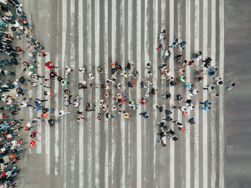 Aerial view of large crowd of people in the shape of an arrow walking down a road with white stripes.