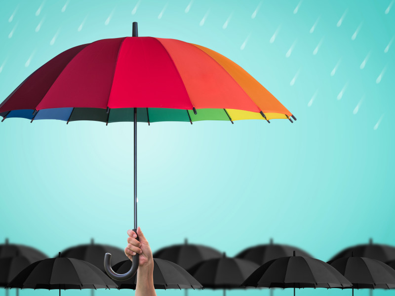 手握彩虹伞在雨中黑色雨伞的海洋之上。