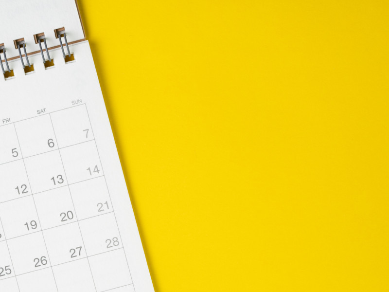 White spiral bound calendar planner against bright yellow background.
