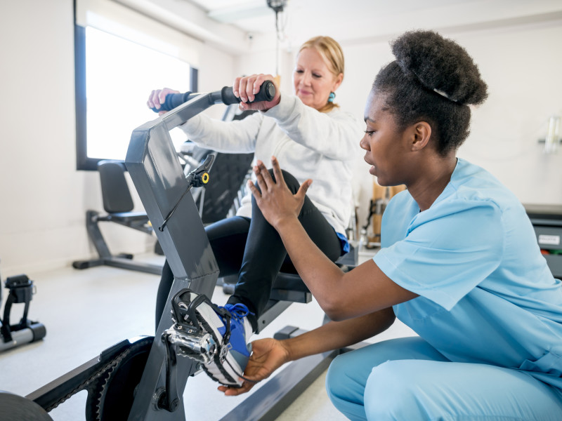 Female PT teaching a senior patient how to use a reclining stationary bike
