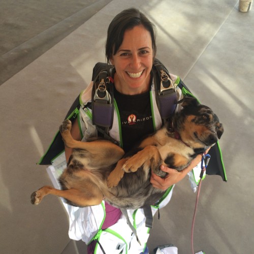 Steph Davis holding dog like a baby while wearing base jumping gear.