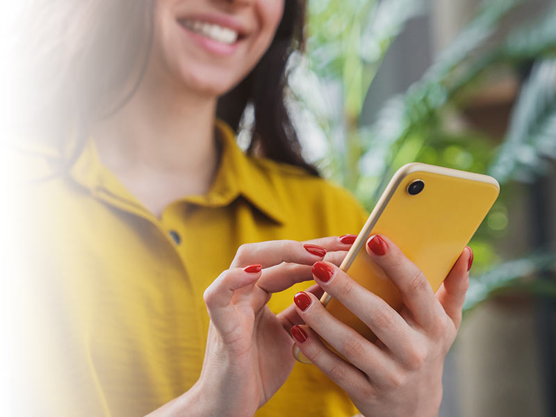 Woman in yellow shirt smiling while using mobile phone