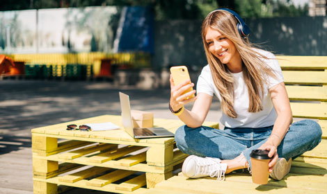 woman sitting on bench using mobile phone and laptop