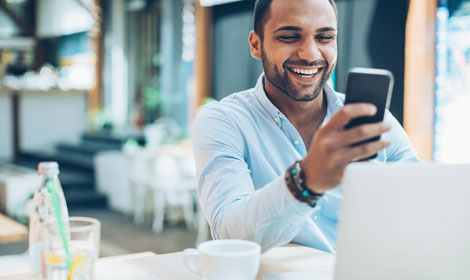 Person smiling looking at mobile in front of a laptop in a restaurant