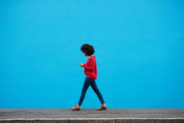 Woman walking with phone in front of a blue background