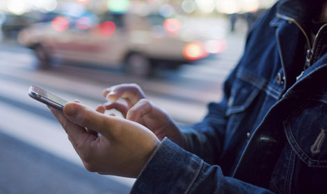 Person using their mobile and messaging while standing on the sidewalk (Blog Post Top Image - 470x280)