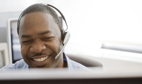 contact center agent with headphones at desk smiling 470x280