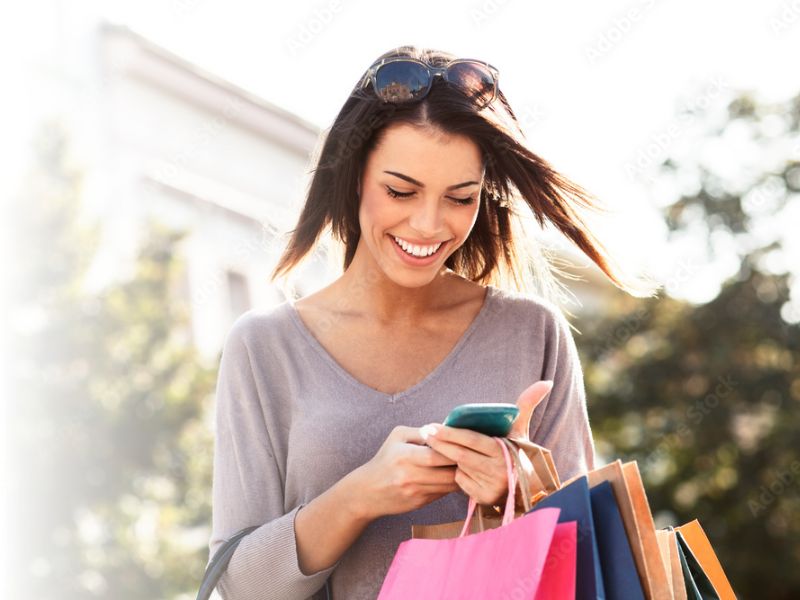 woman smiling looking at mobile phone holding shopping bags