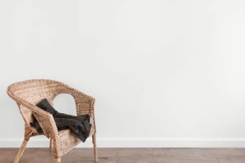 A wicker chair with a folded black blanket in a plain white room with wooden floors.