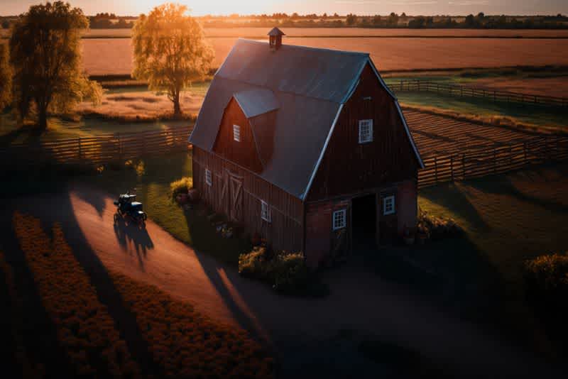 a tall red dutch barn during sunset on a farm with fields in the background