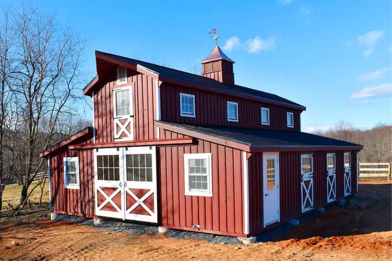 a red monitor barn during mid day on a farm with white fencing in the background