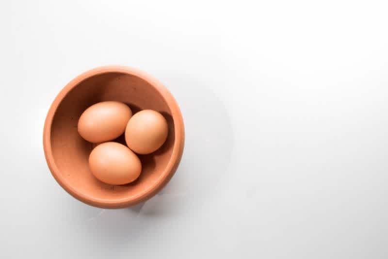 Three brown eggs in a wooden bowl on a white surface