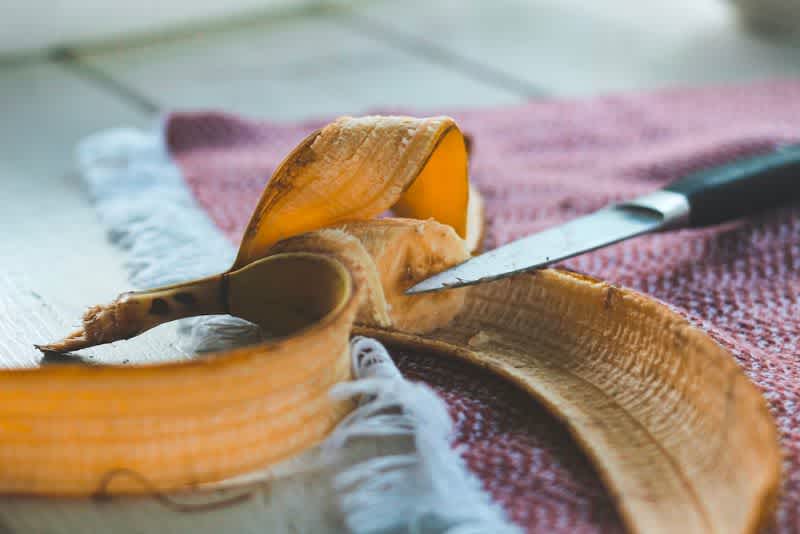 A banana peel with leftover banana inside next to a knife on the kitchen table