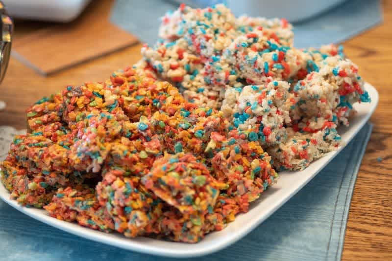 A plate of colorful Rice Krispie treats sitting on a wooden table.