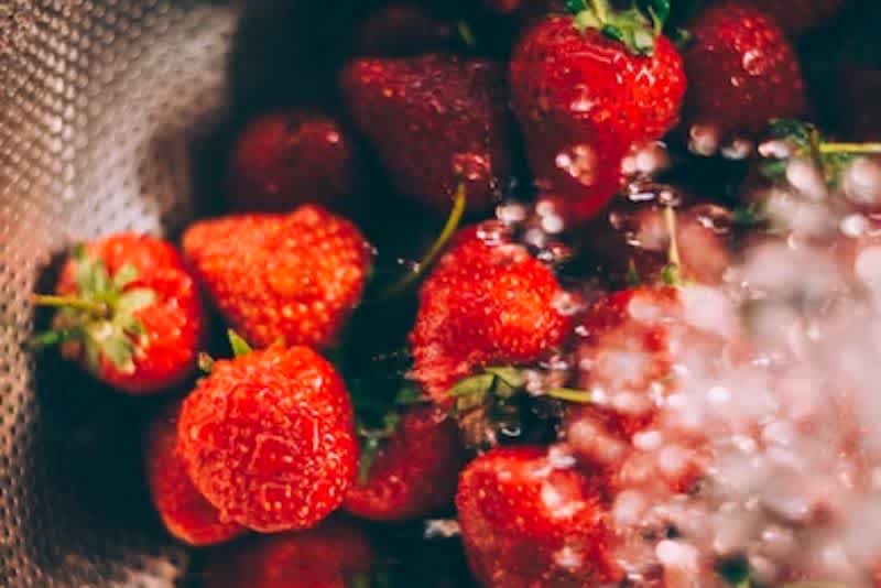 Strawberries under running water inside a colander 