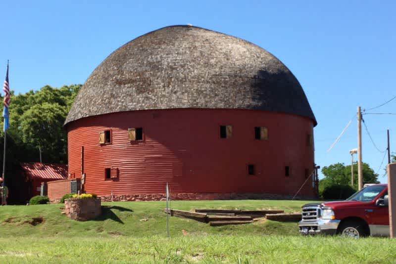 A red round barn next to a red truck on a sunny day