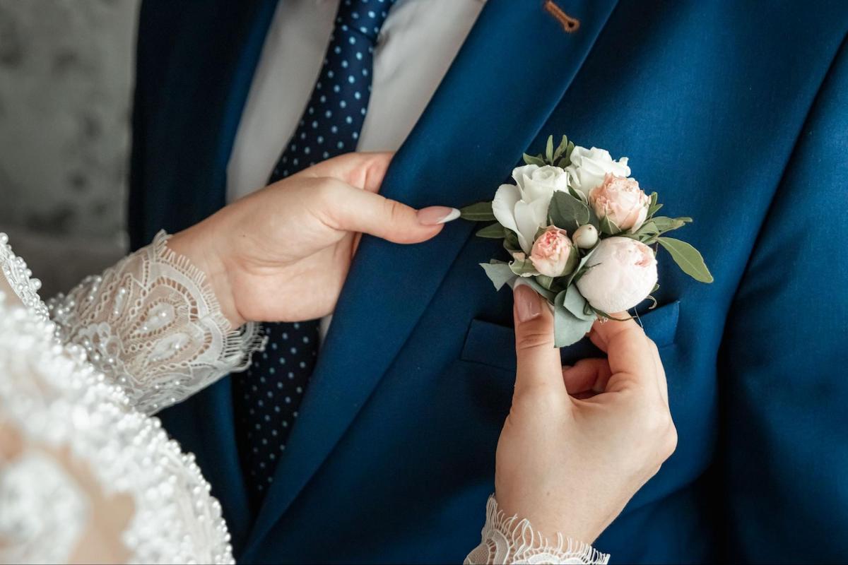 Wedding budget breakdown: woman pinning a boutonniere on the groom
