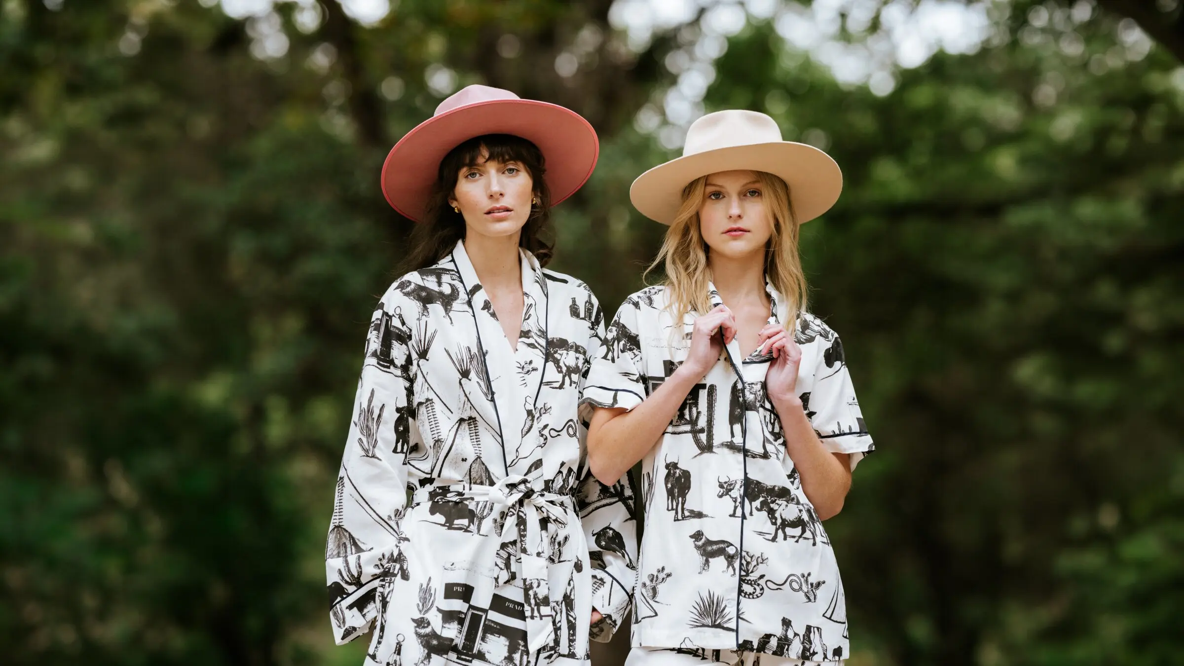 Two models in matching Marfa Toile pajamas and western hats outdoors among trees