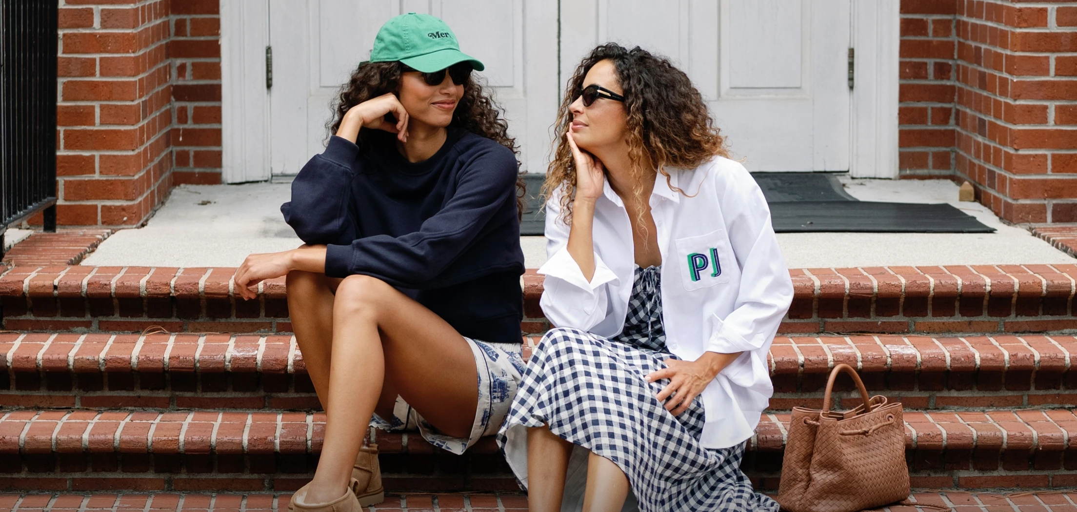 two women sitting on the steps. One woman is wearing a classic charlotte button down white oxford with embroidered initials on the pocket