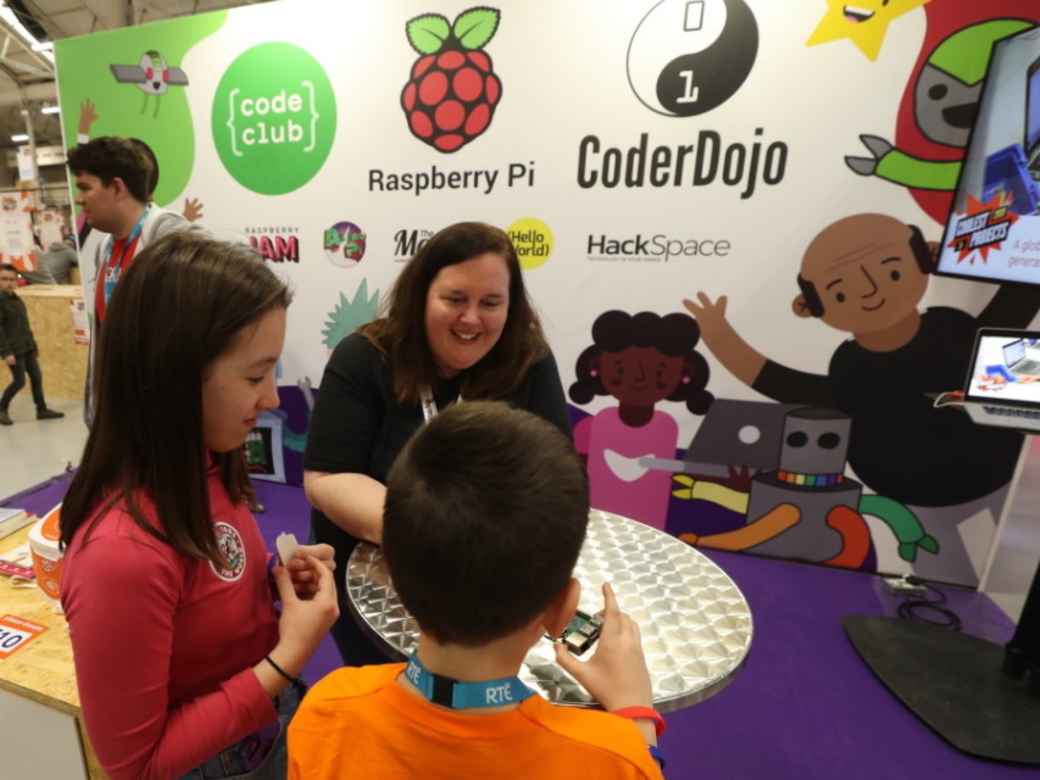 A staff member talking with children in front of a CoderDojo and Raspberry Pi branded stand