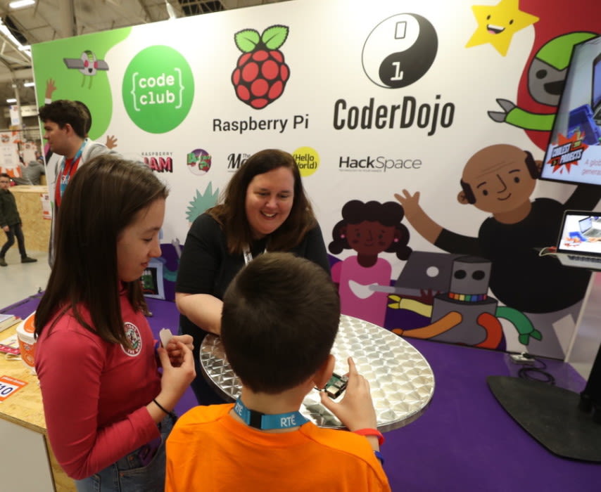 A staff member talking with children in front of a CoderDojo and Raspberry Pi branded stand