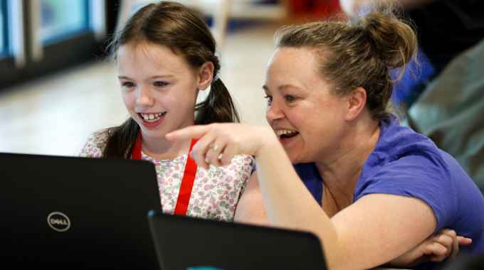Woman and girl laughing and pointing at a laptop
